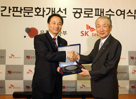 Myung Gon Kim, Minister of Culture and Tourism, is shown shaking a hand with Jung Nam Cho, vice-chairman of SK Telecom.
